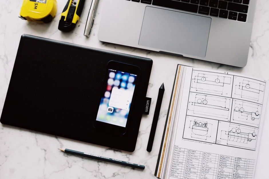 Gros plan sur un carnet avec des croquis de wireframe et un smartphone posé sur un bureau en bois.